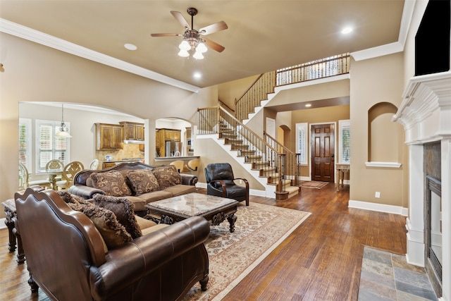 living room with dark wood-type flooring, a high ceiling, ceiling fan, ornamental molding, and a fireplace