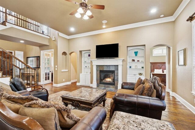 living room featuring hardwood / wood-style floors, a towering ceiling, crown molding, and a tiled fireplace