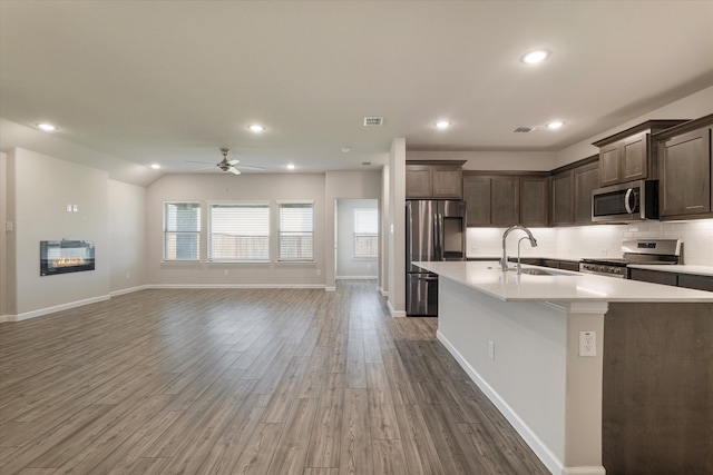 kitchen with stainless steel appliances, ceiling fan, sink, dark hardwood / wood-style floors, and an island with sink