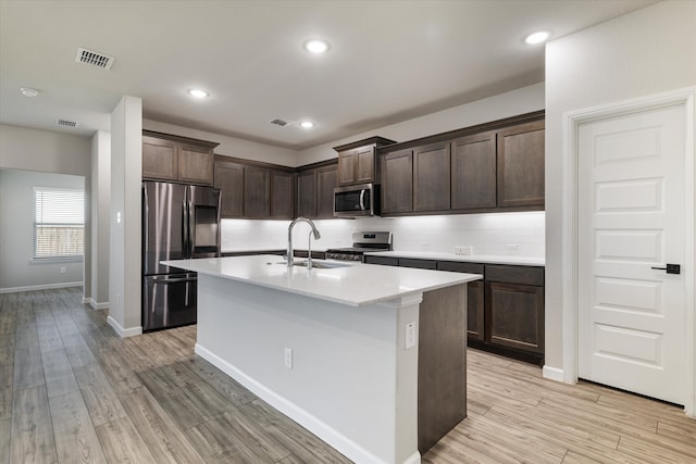 kitchen featuring appliances with stainless steel finishes, light wood-type flooring, dark brown cabinetry, sink, and a center island with sink