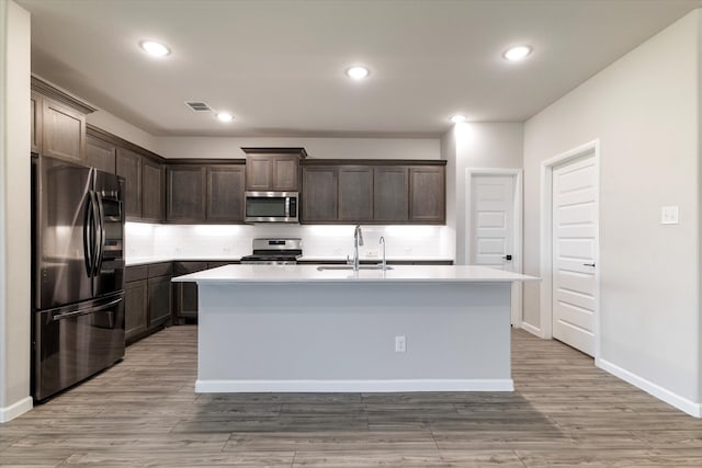 kitchen with sink, an island with sink, dark brown cabinets, and appliances with stainless steel finishes