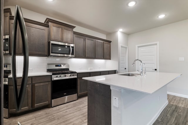 kitchen with sink, stainless steel appliances, light hardwood / wood-style flooring, dark brown cabinets, and a center island with sink