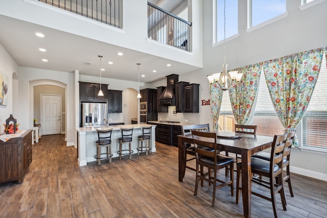 dining space with a wealth of natural light, a towering ceiling, dark wood-type flooring, and a notable chandelier