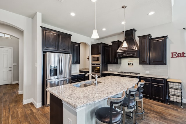 kitchen featuring pendant lighting, custom exhaust hood, a kitchen island with sink, sink, and appliances with stainless steel finishes