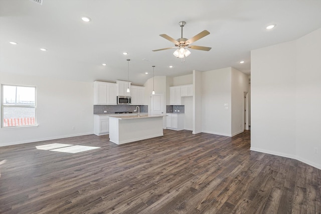 kitchen with a kitchen island with sink, white cabinetry, open floor plan, light countertops, and stainless steel microwave