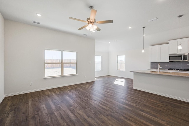 unfurnished living room featuring a ceiling fan, baseboards, visible vents, and dark wood-type flooring