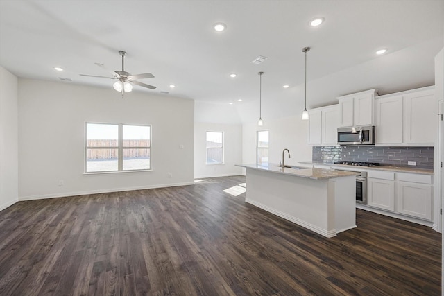 kitchen with a kitchen island with sink, white cabinets, open floor plan, appliances with stainless steel finishes, and decorative light fixtures