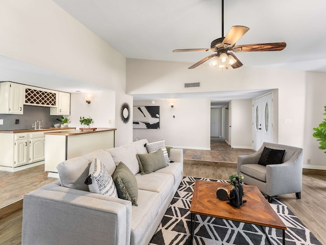 living room with ceiling fan, light hardwood / wood-style flooring, high vaulted ceiling, and sink