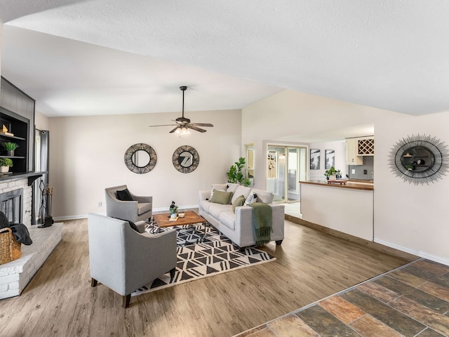 living room with ceiling fan, wood-type flooring, vaulted ceiling, and a brick fireplace