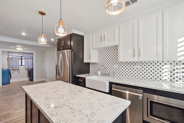 kitchen featuring appliances with stainless steel finishes, sink, white cabinets, light hardwood / wood-style floors, and hanging light fixtures