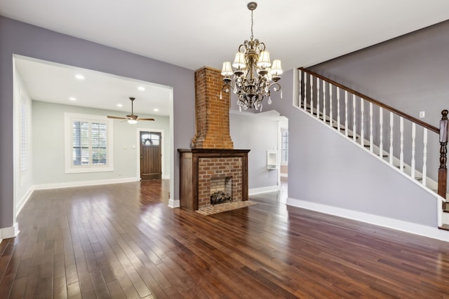 unfurnished living room featuring a fireplace, dark wood-type flooring, and ceiling fan with notable chandelier