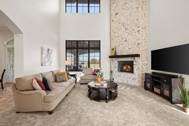 living room featuring light colored carpet, a towering ceiling, a stone fireplace, and french doors