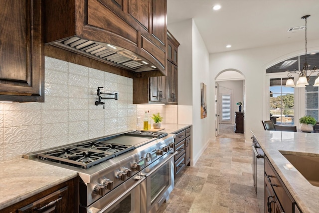 kitchen featuring dark brown cabinetry, custom exhaust hood, decorative light fixtures, range with two ovens, and an inviting chandelier