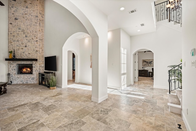 living room featuring a notable chandelier, a towering ceiling, a stone fireplace, and beam ceiling