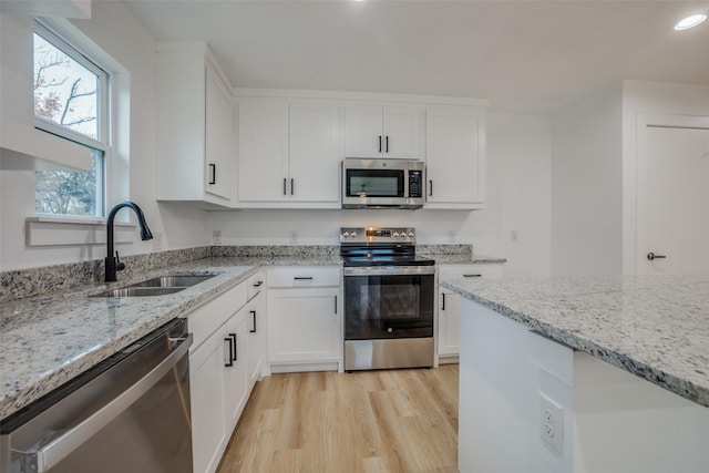 kitchen featuring sink, light stone countertops, appliances with stainless steel finishes, light hardwood / wood-style floors, and white cabinetry