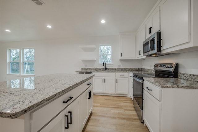 kitchen with a wealth of natural light, light hardwood / wood-style flooring, white cabinets, and appliances with stainless steel finishes