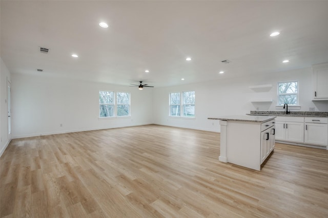 kitchen featuring a center island, ceiling fan, light wood-type flooring, light stone counters, and white cabinetry