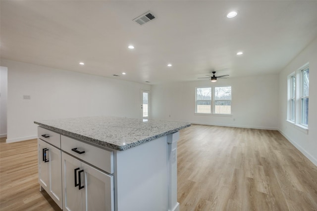 kitchen featuring white cabinets, ceiling fan, a kitchen island, light stone countertops, and light hardwood / wood-style floors