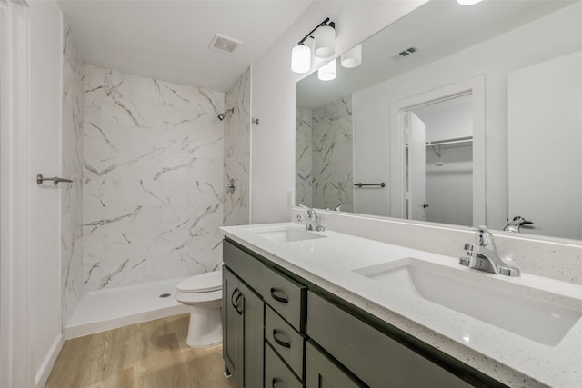 bathroom with toilet, wood-type flooring, vanity, and a tile shower