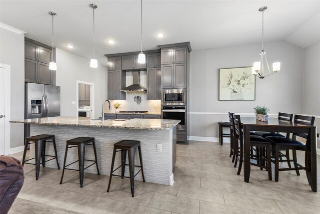 kitchen with sink, wall chimney exhaust hood, hanging light fixtures, stainless steel appliances, and a breakfast bar