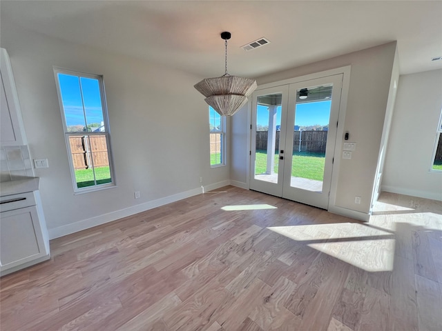 unfurnished dining area featuring a healthy amount of sunlight, french doors, and light hardwood / wood-style flooring