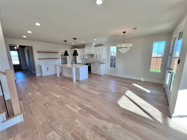 kitchen featuring white cabinetry, a kitchen island with sink, a notable chandelier, and light hardwood / wood-style floors