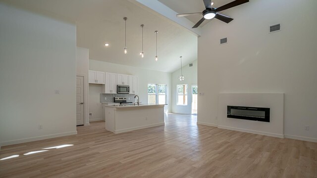 unfurnished living room featuring ceiling fan with notable chandelier, light wood-type flooring, sink, and high vaulted ceiling