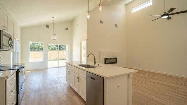 kitchen with appliances with stainless steel finishes, light hardwood / wood-style flooring, high vaulted ceiling, white cabinets, and an island with sink