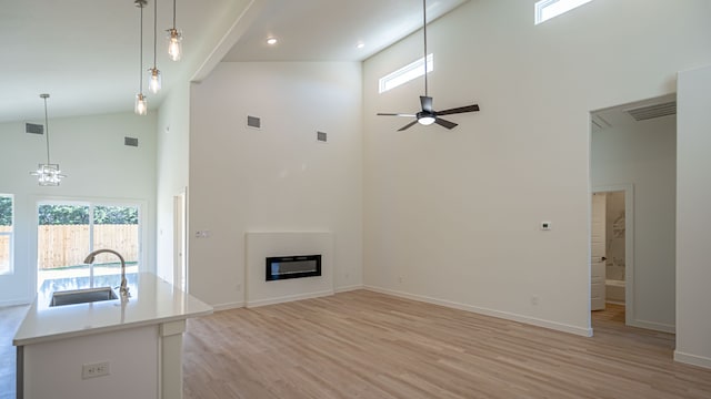 unfurnished living room with sink, high vaulted ceiling, ceiling fan with notable chandelier, and light hardwood / wood-style flooring