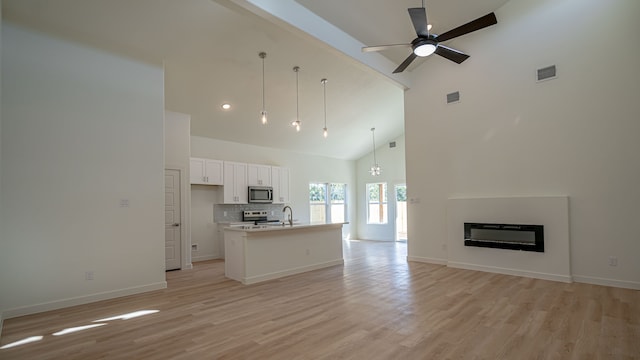 kitchen with white cabinetry, high vaulted ceiling, pendant lighting, a kitchen island with sink, and appliances with stainless steel finishes