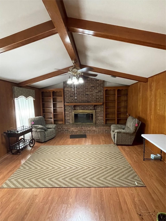 living room featuring lofted ceiling with beams, wooden walls, light wood-style floors, built in features, and a brick fireplace