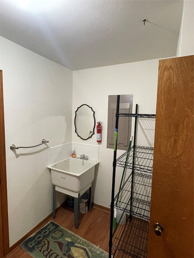 bathroom with a textured ceiling, electric panel, baseboards, and wood finished floors