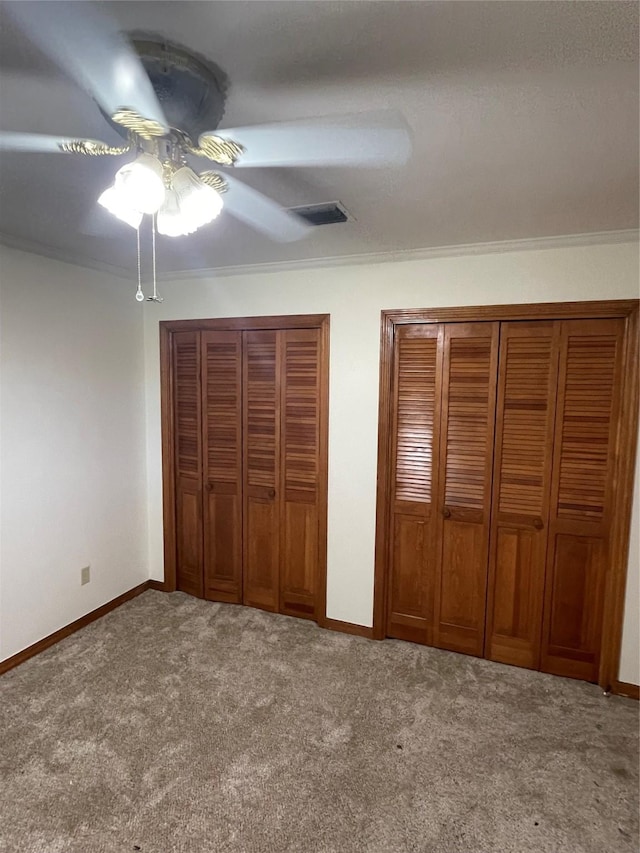 unfurnished bedroom featuring multiple closets, carpet flooring, crown molding, and baseboards