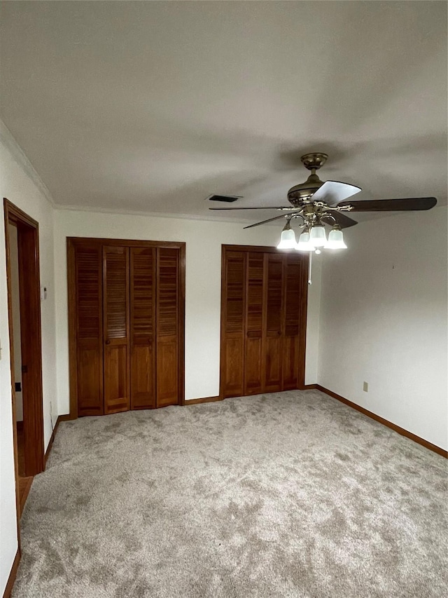 unfurnished bedroom featuring visible vents, baseboards, ceiling fan, carpet flooring, and two closets