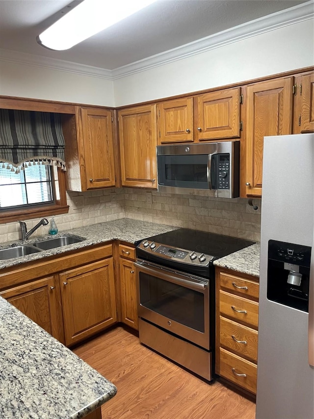 kitchen featuring appliances with stainless steel finishes, brown cabinetry, a sink, and crown molding