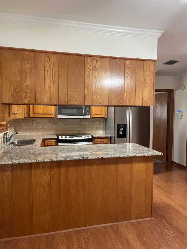 kitchen with stainless steel appliances, a peninsula, a sink, and brown cabinets