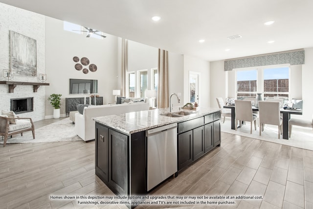 kitchen with sink, light hardwood / wood-style flooring, stainless steel dishwasher, a fireplace, and an island with sink