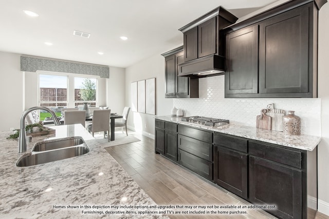 kitchen featuring light stone countertops, dark brown cabinetry, stainless steel gas cooktop, sink, and light hardwood / wood-style floors