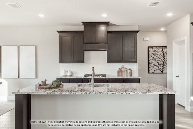 kitchen with a kitchen island with sink, dark brown cabinets, and light hardwood / wood-style flooring