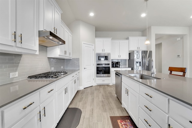 kitchen with appliances with stainless steel finishes, light wood-type flooring, sink, decorative light fixtures, and white cabinetry