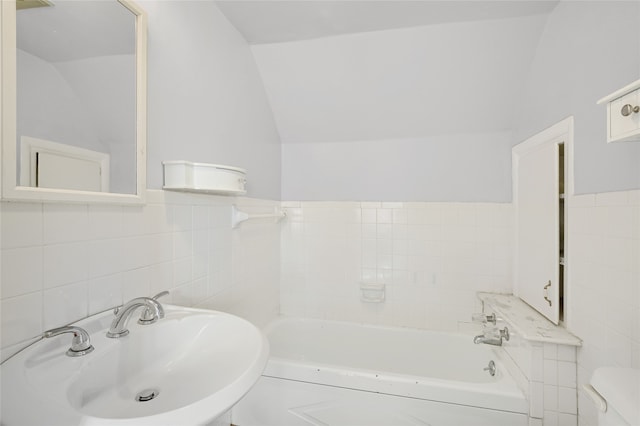 bathroom with a bathtub, vaulted ceiling, sink, tile walls, and toilet