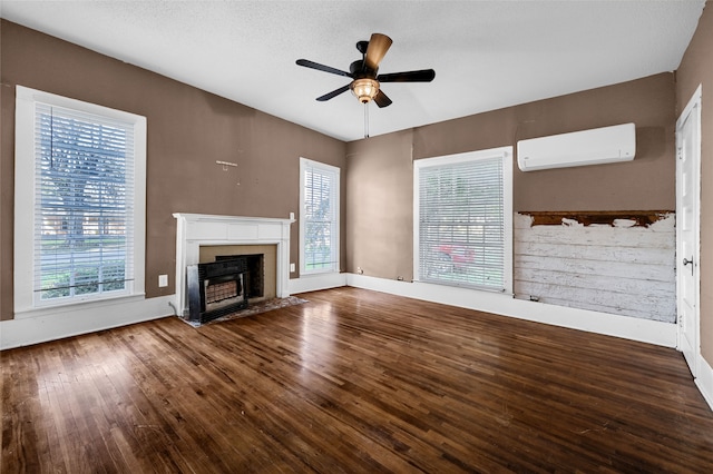 unfurnished living room featuring wood-type flooring, plenty of natural light, a wall mounted AC, and ceiling fan