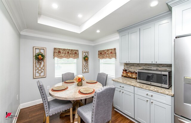 dining area with a raised ceiling, crown molding, and dark wood-type flooring