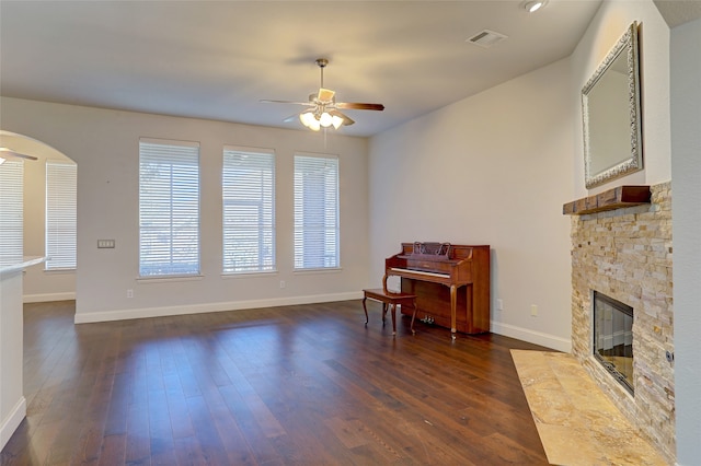 interior space with a stone fireplace, ceiling fan, and dark wood-type flooring