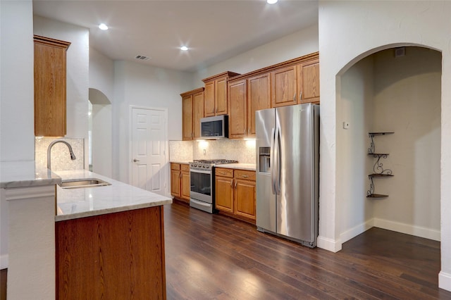 kitchen with light stone countertops, sink, stainless steel appliances, tasteful backsplash, and dark hardwood / wood-style flooring