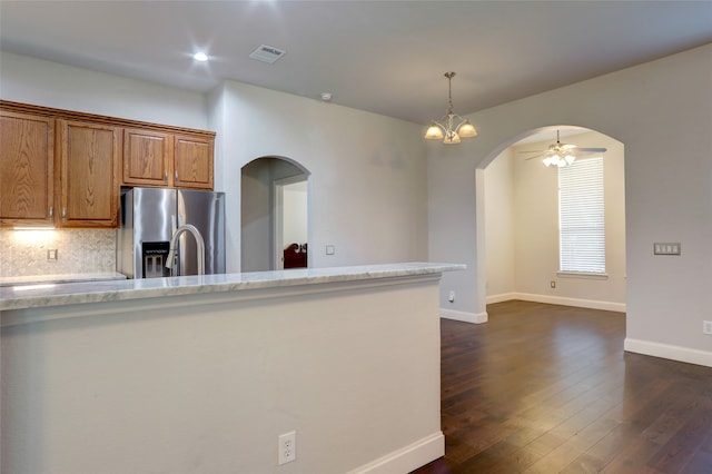 kitchen featuring hanging light fixtures, dark hardwood / wood-style flooring, backsplash, stainless steel fridge, and ceiling fan with notable chandelier