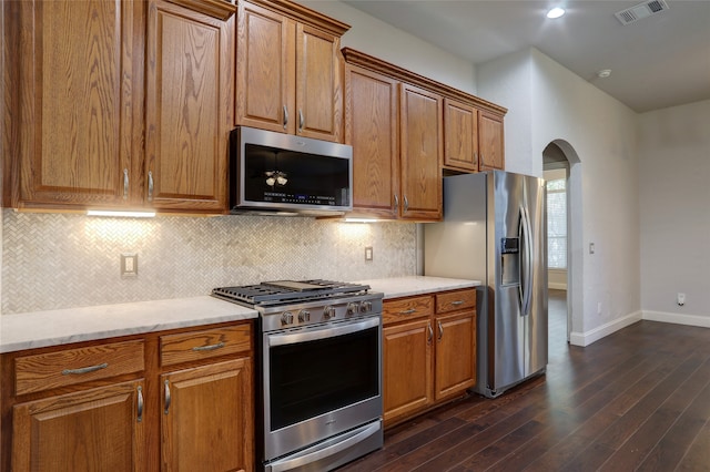 kitchen featuring backsplash, dark hardwood / wood-style floors, light stone counters, and stainless steel appliances