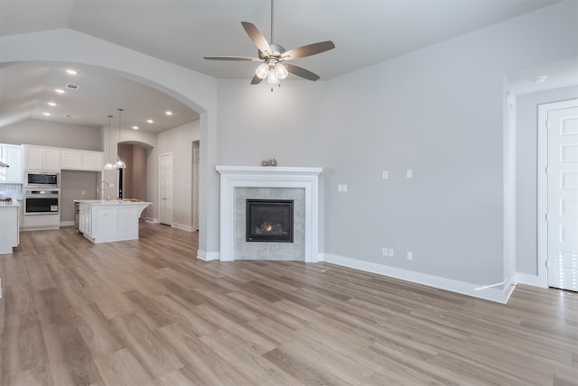 unfurnished living room featuring a tile fireplace, ceiling fan, light hardwood / wood-style floors, and vaulted ceiling