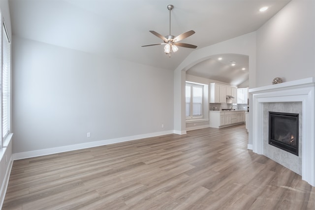 unfurnished living room featuring ceiling fan, a fireplace, light hardwood / wood-style floors, and vaulted ceiling