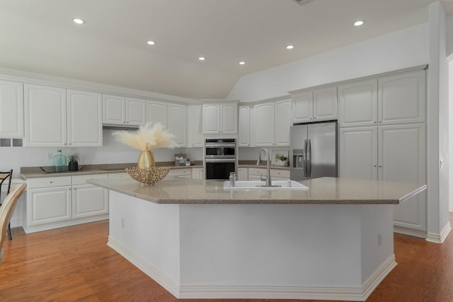 kitchen with stainless steel appliances, an island with sink, light stone countertops, sink, and white cabinetry